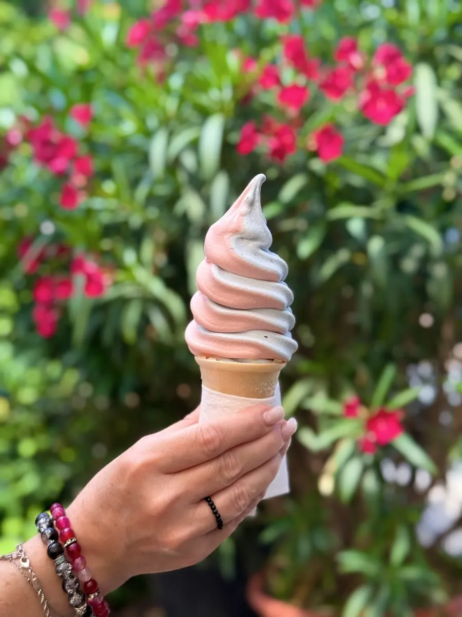 Softeis-Hörnchen mit hellem Frucht-Swirl vor blühendem Oleander